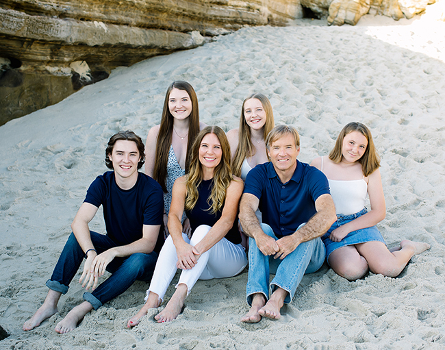 A family posing on a sandy beach with a rocky cliff in the background.