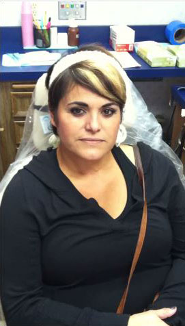 A woman with short hair, wearing glasses, sitting at a dental chair.