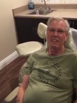 An elderly man sitting in a dental chair with a smile on his face.