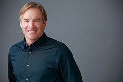 The image shows a man posing for a portrait with a neutral background.