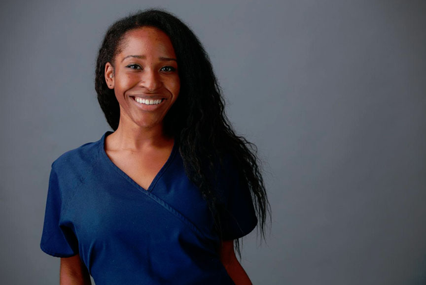 The image shows a smiling woman wearing a scrubs uniform, posing against a neutral background.