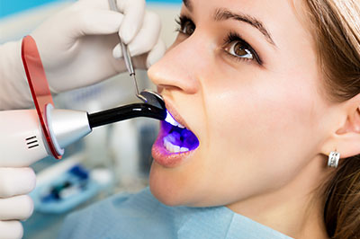 The image shows a person receiving dental care, with a dentist using a device to clean their teeth while the patient s mouth is open.