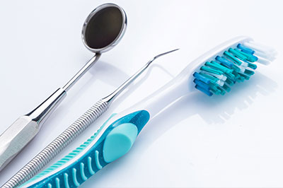A photograph of dental instruments including a toothbrush with blue bristles, a pair of scissors, and other dental tools arranged beside each other on a white background.