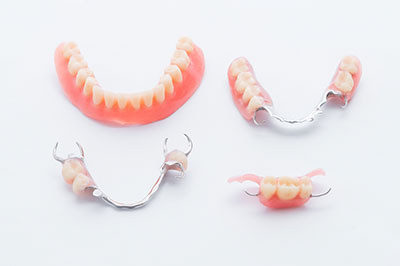 The image shows three pairs of dentures displayed on a white surface, with two pairs featuring a set of upper teeth and one pair showing lower teeth.