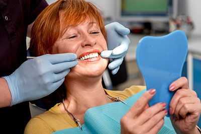 A woman sitting in a dental chair with a smile on her face, receiving dental care, while holding a blue model tooth.